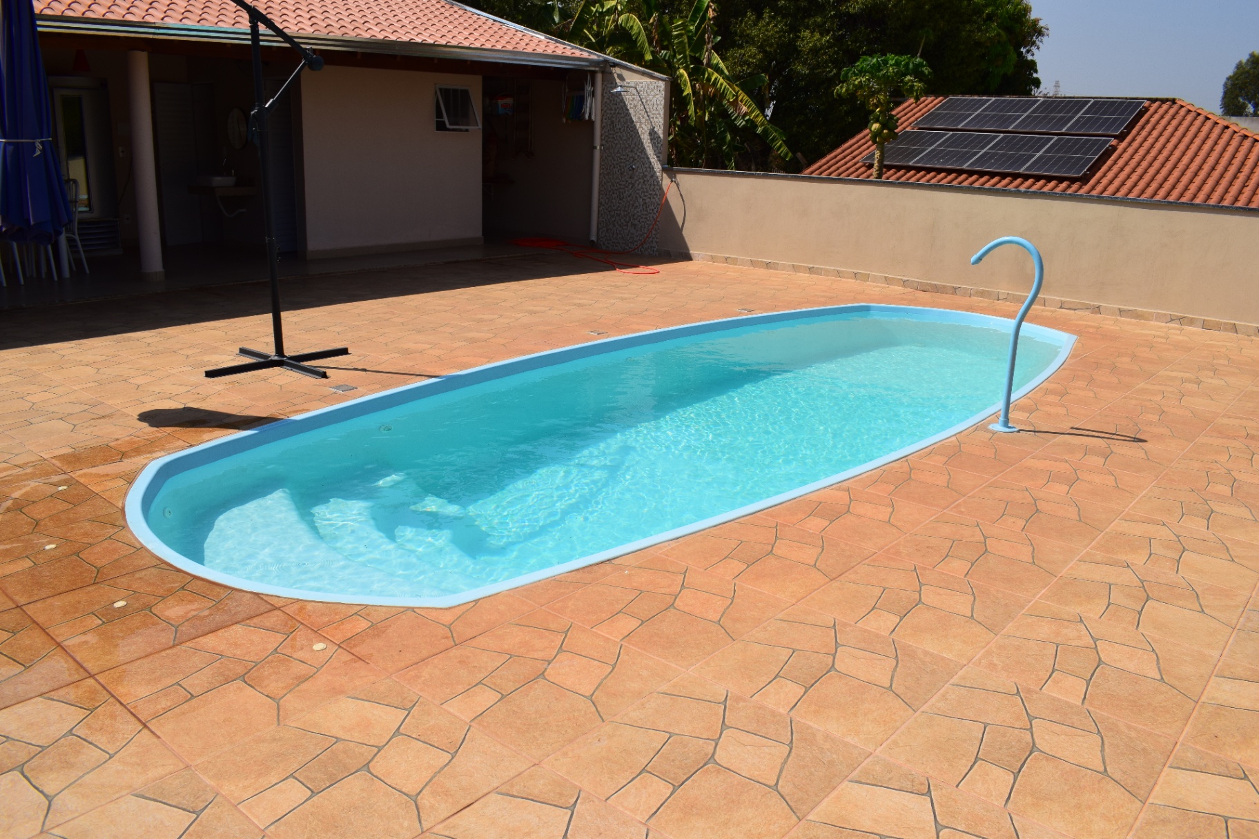 Piscina oval branca em área de lazer com placas solares ao fundo