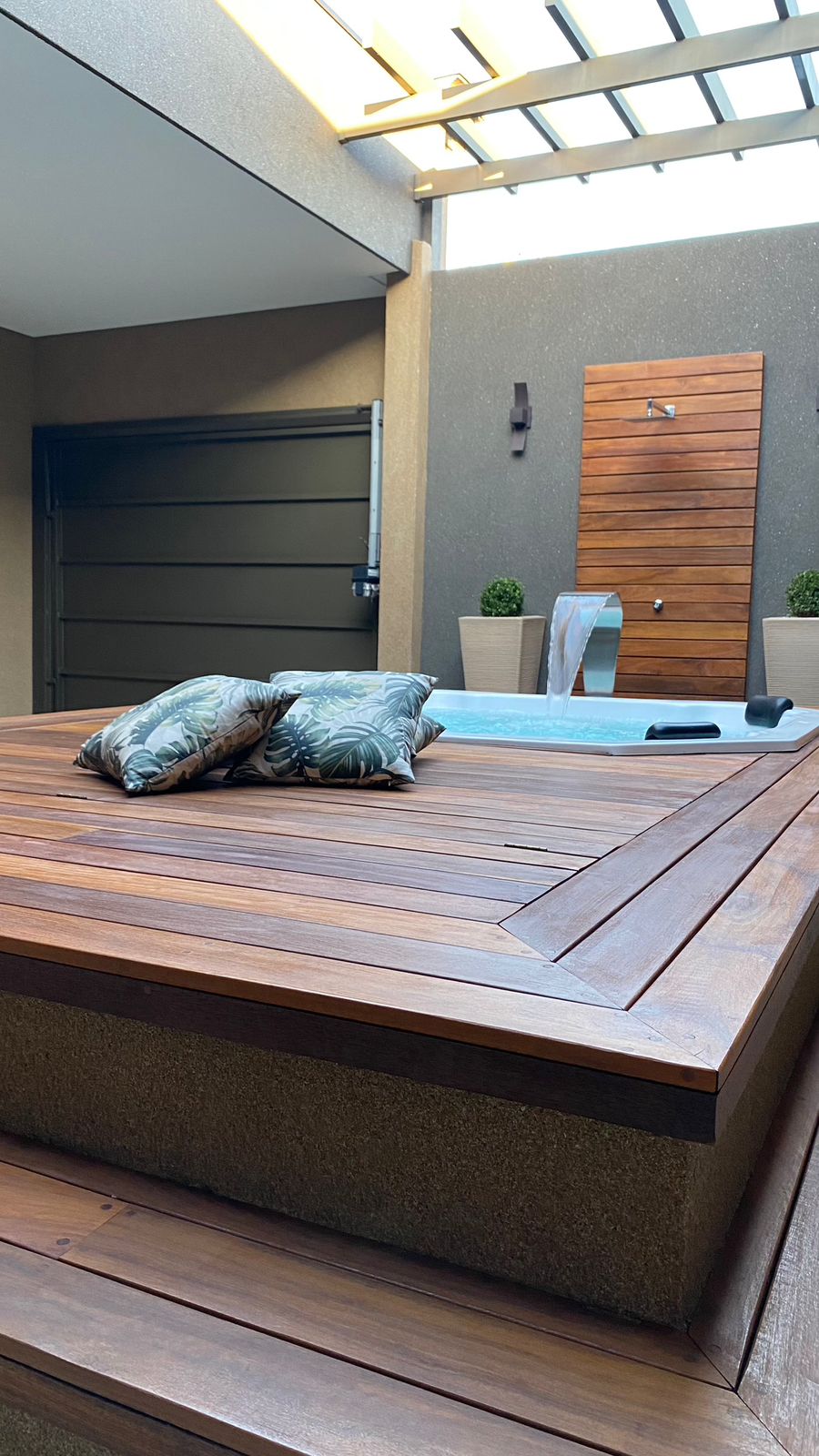 Spa em deck de madeira com pergolado e cascata em aço