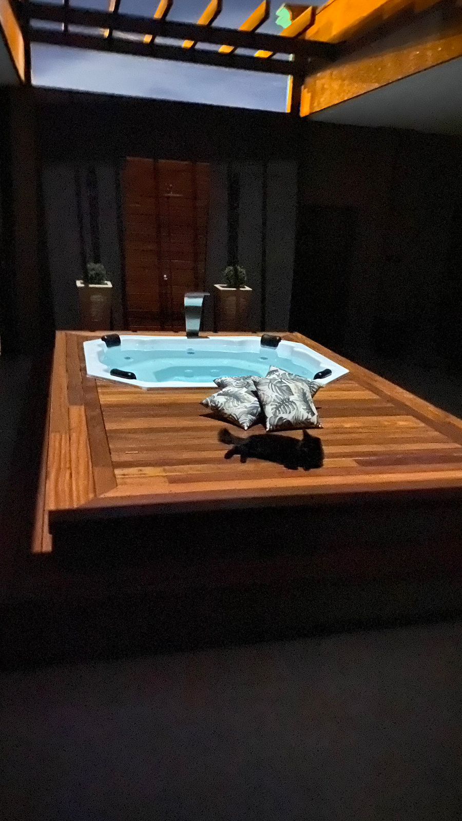 Spa iluminado à noite em deck de madeira sob pergolado
